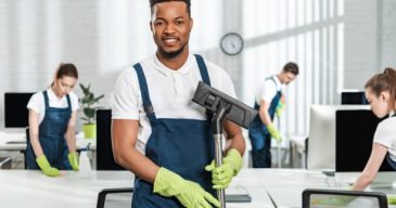 smiling african american cleaner holding vacuum cleaner brush near team of multicultural colleagues